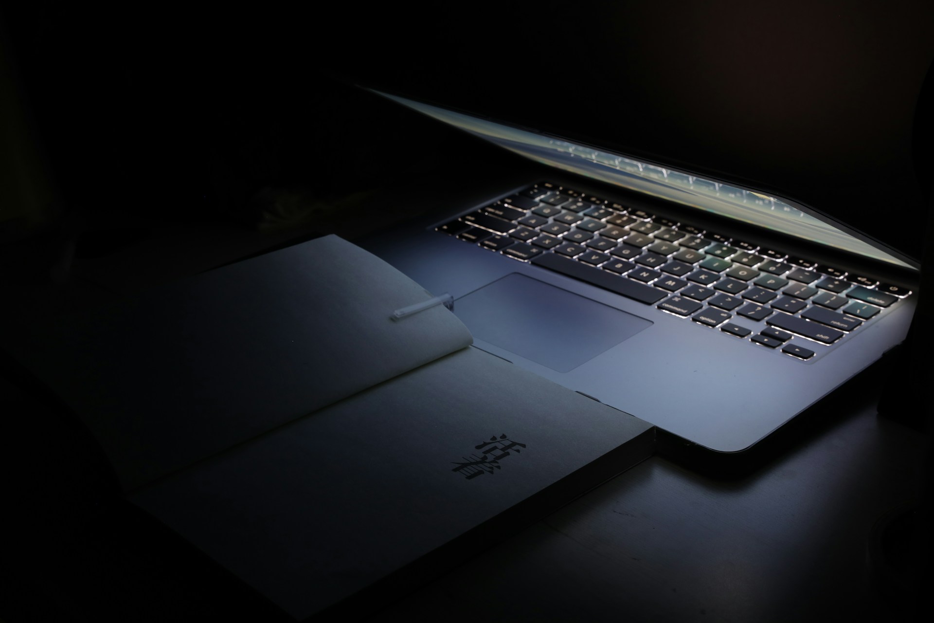 Een op een toetsenbord verlicht laptop met een open boek met Aziatische tekens in een donkere omgeving.